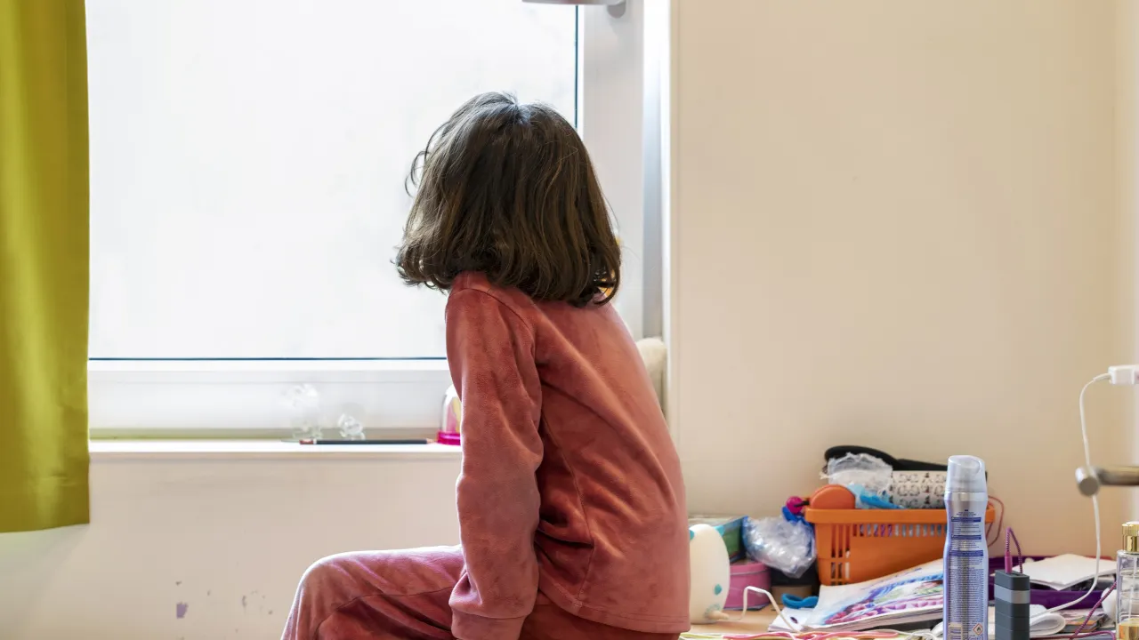 Een meisje in de opvang kijkt door het raam naar buiten