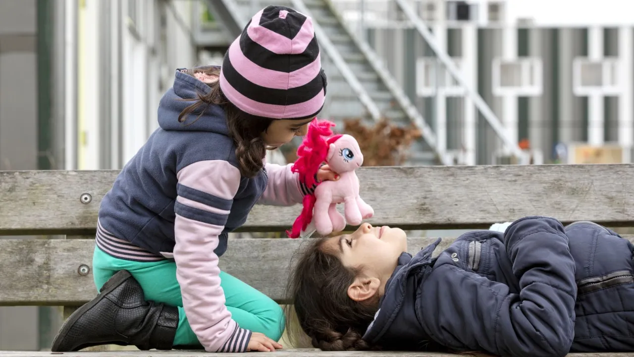 Twee jonge meisjes spelen op een bankje buiten bij AZC Drachten