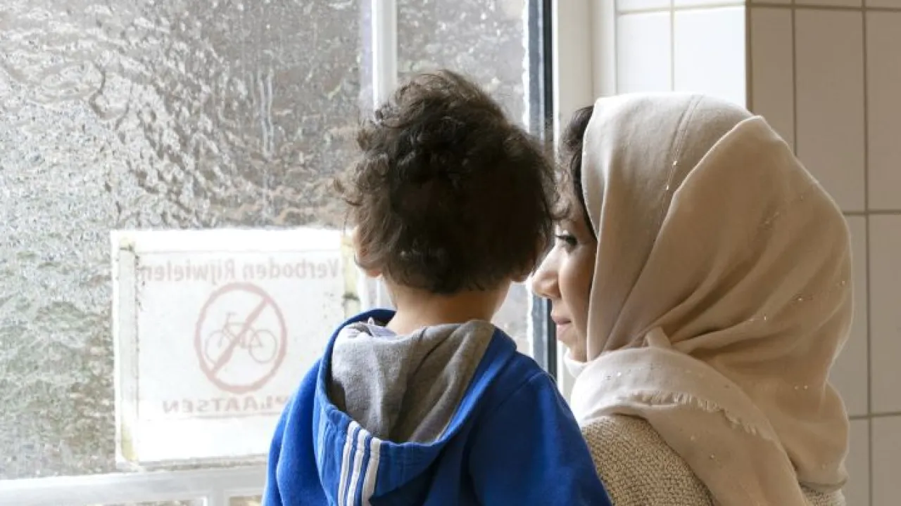 Moeder en kind kijken samen uit het raam in azc