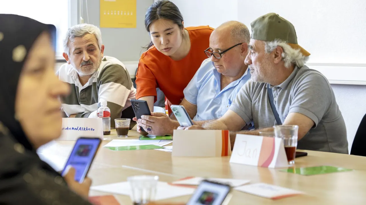 Vluchtelingen zitten aan tafel en krijgen voorlichting in digitale vaardigheden