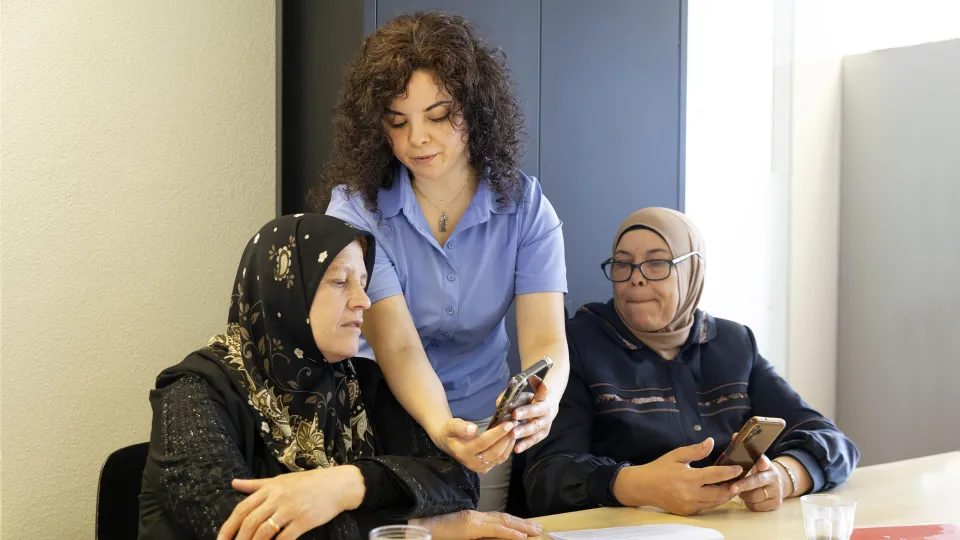 Een vrijwilliger helpt met het programma DigiKlik twee vrouwelijke vluchtelingen met hun digitale vaardigheden. 