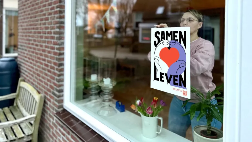 Vrouw hangt vluchtelingenwerk poster voor het raam
