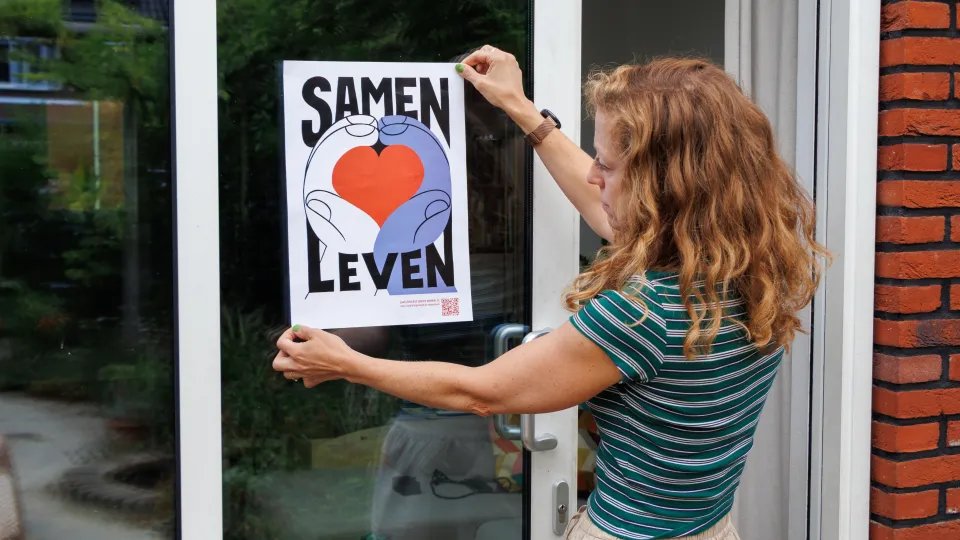 Een vrouw kijkt hoe de poster zou hangen aan het raam