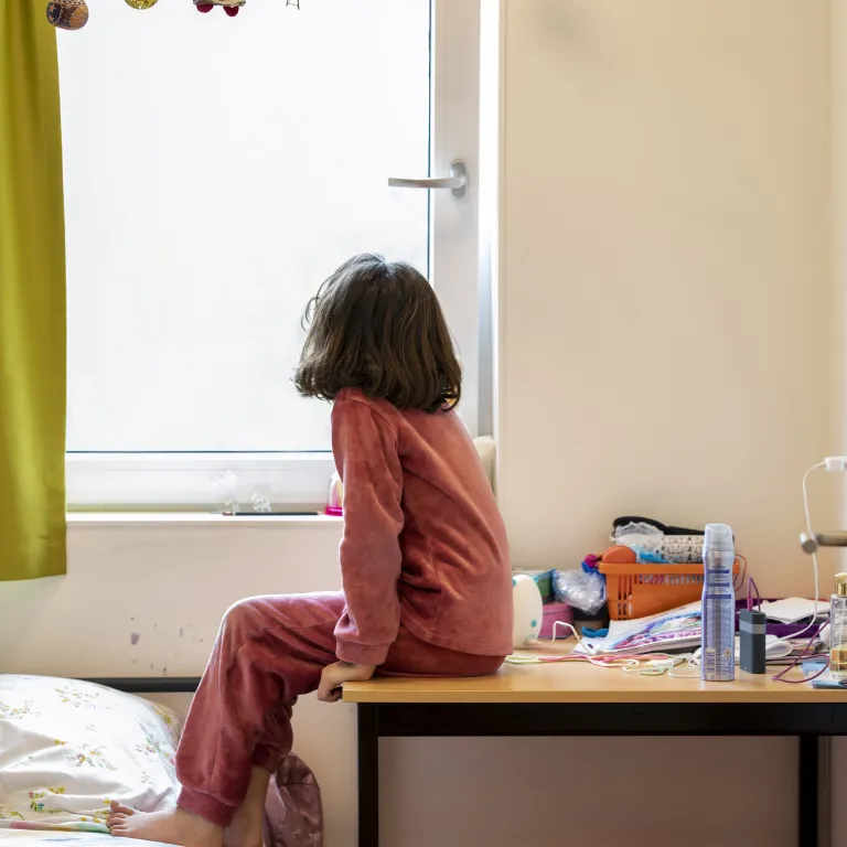 Een meisje in de opvang kijkt door het raam naar buiten