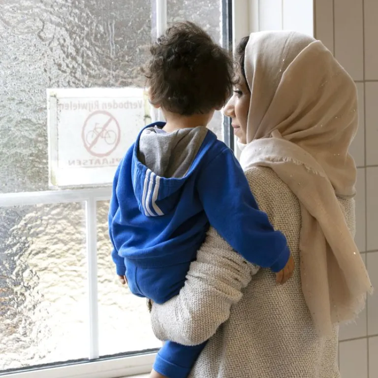 Moeder en kind kijken samen uit het raam in azc