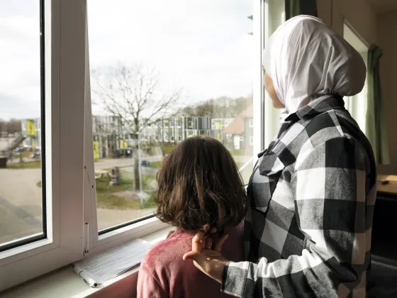 Een moeder en kind kijken uit het raam in een asielzoekerscentrum
