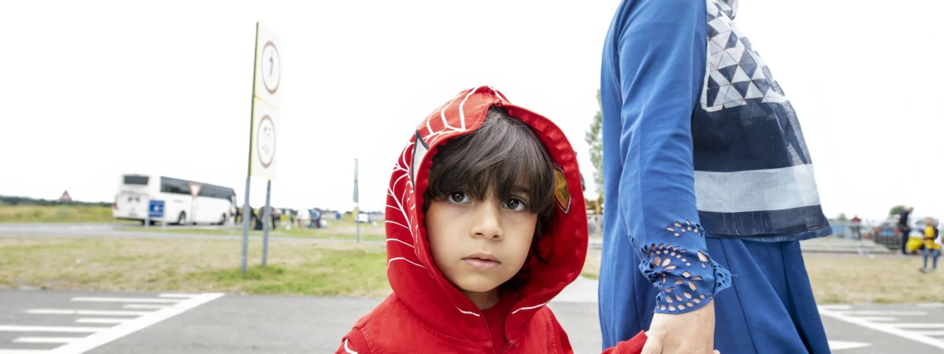 Een kindje kijkt verdrietig in de camera, aan de hand van haar moeder