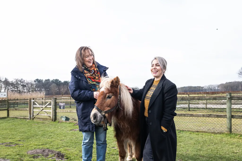 Vrijwilliger Cora en Nederlandse Neba staan in weiland met pony