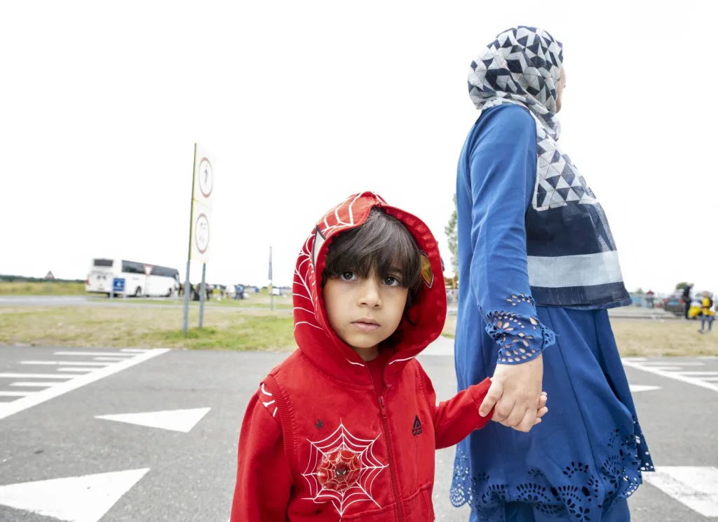 Een kindje kijkt verdrietig in de camera, aan de hand van haar moeder