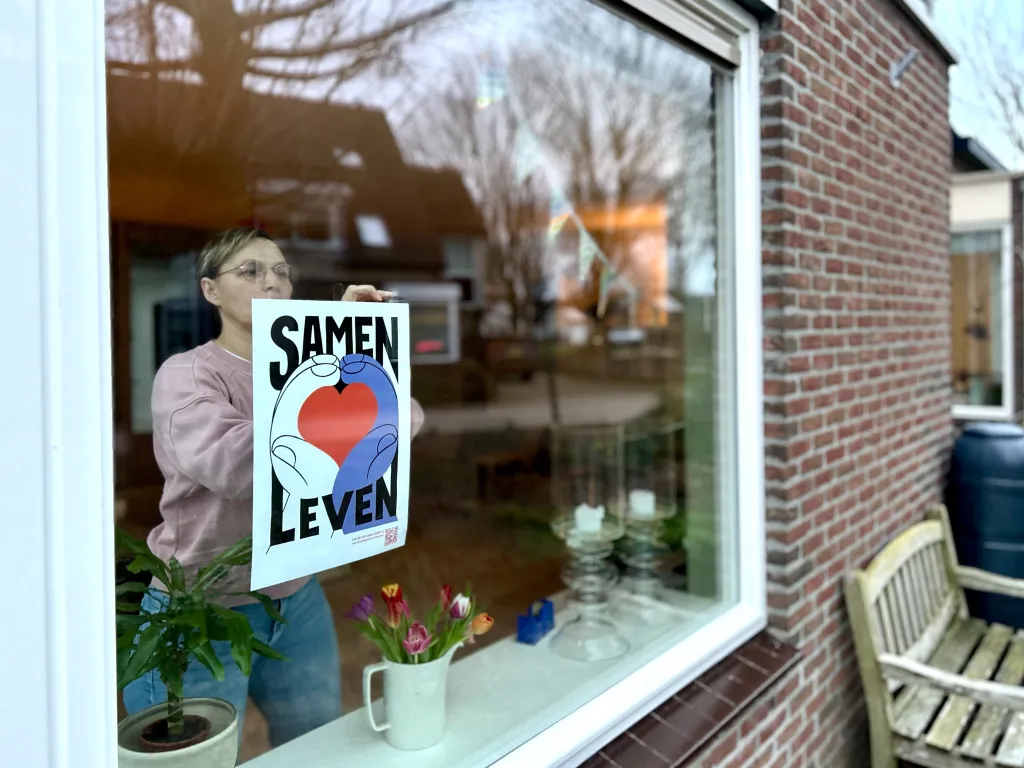 Een vrouw uit Houten hangt de Samen Leven poster zichtbaar op haar raam.