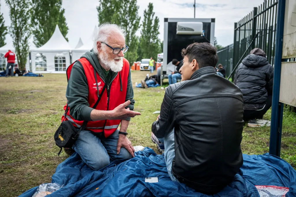 Een vrijwilliger geeft voorlichting aan een asielzoeker voor de poorten van Ter Apel